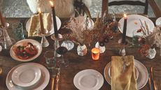 An autumnal tablescape with glasses, plates, candles and dried flowers.