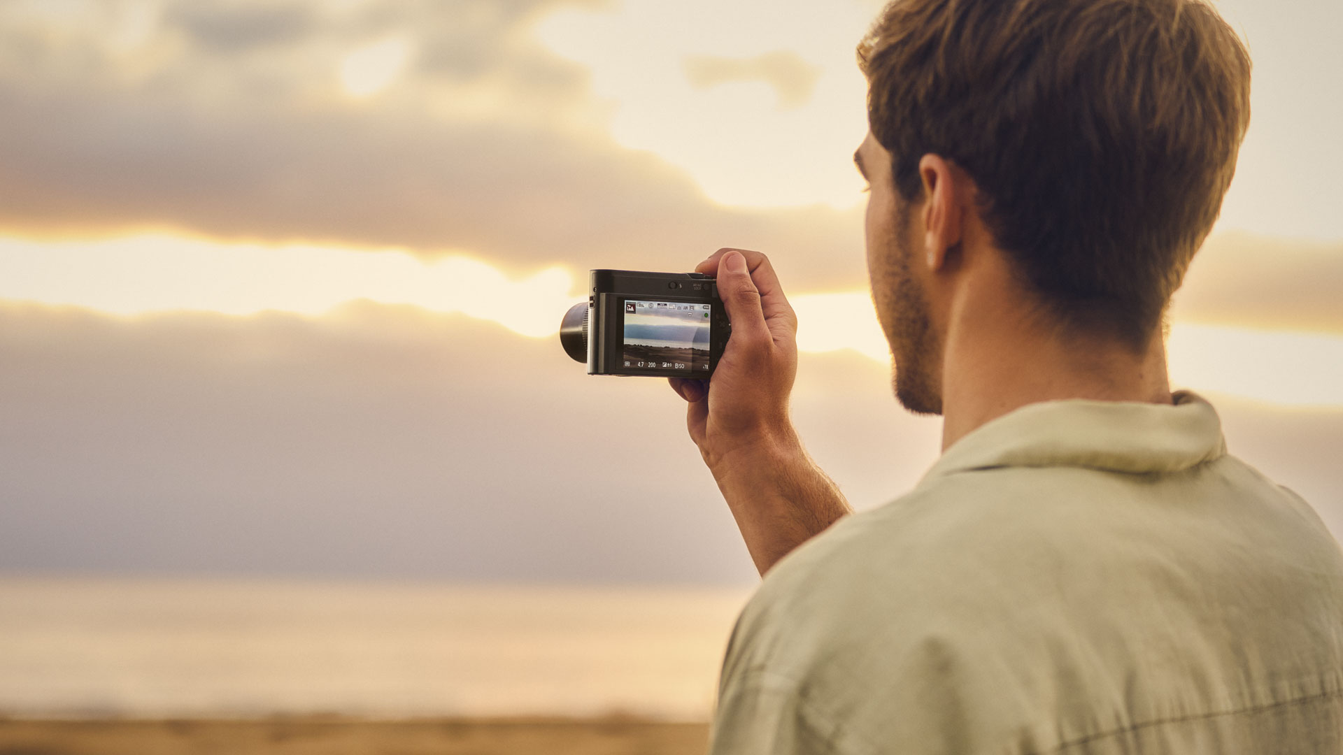 Panasonic Lumix TZ300 travel compact camera in man's hand, who is pointing the camera towards a sunset