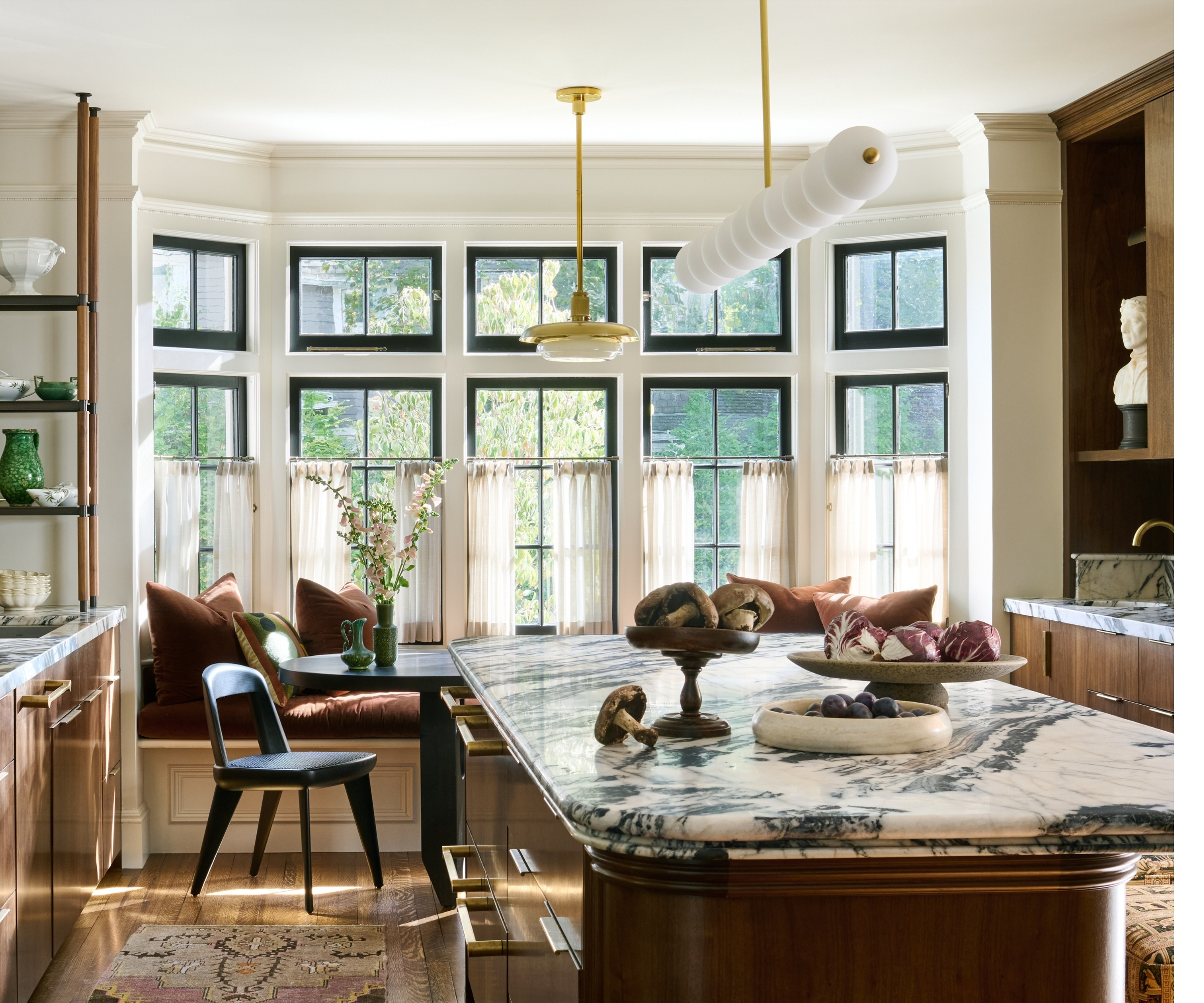 A large kitchen with dark wood cabinets, marble countertops, and a bay window filled with banquette seating