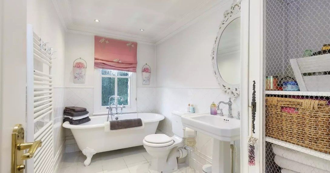 An en suite bathroom shows a white bathroom with an old fashioned sink and cabinet filled with towels