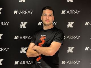 A man, arms folded, in front of a wall with the K-array logo.