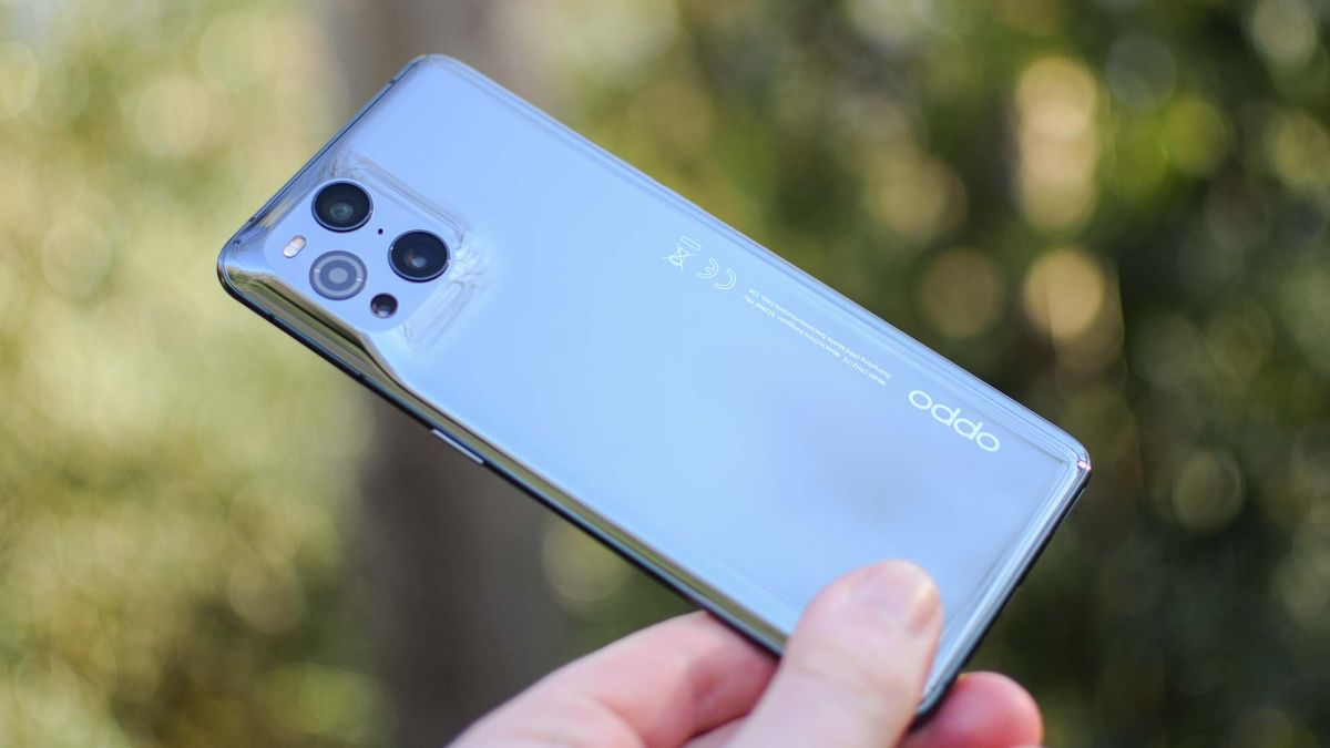 The Oppo Find X3 Pro, held with its back to the camera in front of a green background.