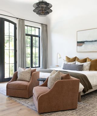 A large bedroom with an arched glass door leading outside and two pink armchairs at the foot of the bed