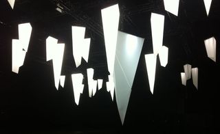 Multiple shard-like tetrahedral lights in different sizes suspended from a ceiling in a dark room