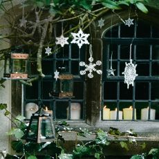 Christmas snowflake window decorations hang amongst green foliage 