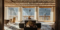 A sun-filled chalet's hall features brutalist rocky floors, wooden ceilings, and modern rustic furniture.