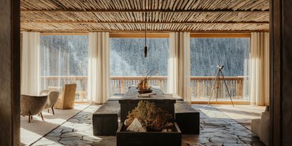 A sun-filled chalet's hall features brutalist rocky floors, wooden ceilings, and modern rustic furniture.