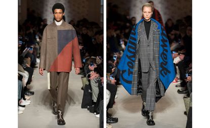 Catwalk view of two models wearing looks from OAMC's collection. One model is wearing a white top, brown, blue and red jacket, brown trousers, white belt and brown boots. And the second model is wearing a black top, grey grid style suit, grey plaid coat, blue shawl with black writing and black boots. There are people seated on both sides of the catwalk