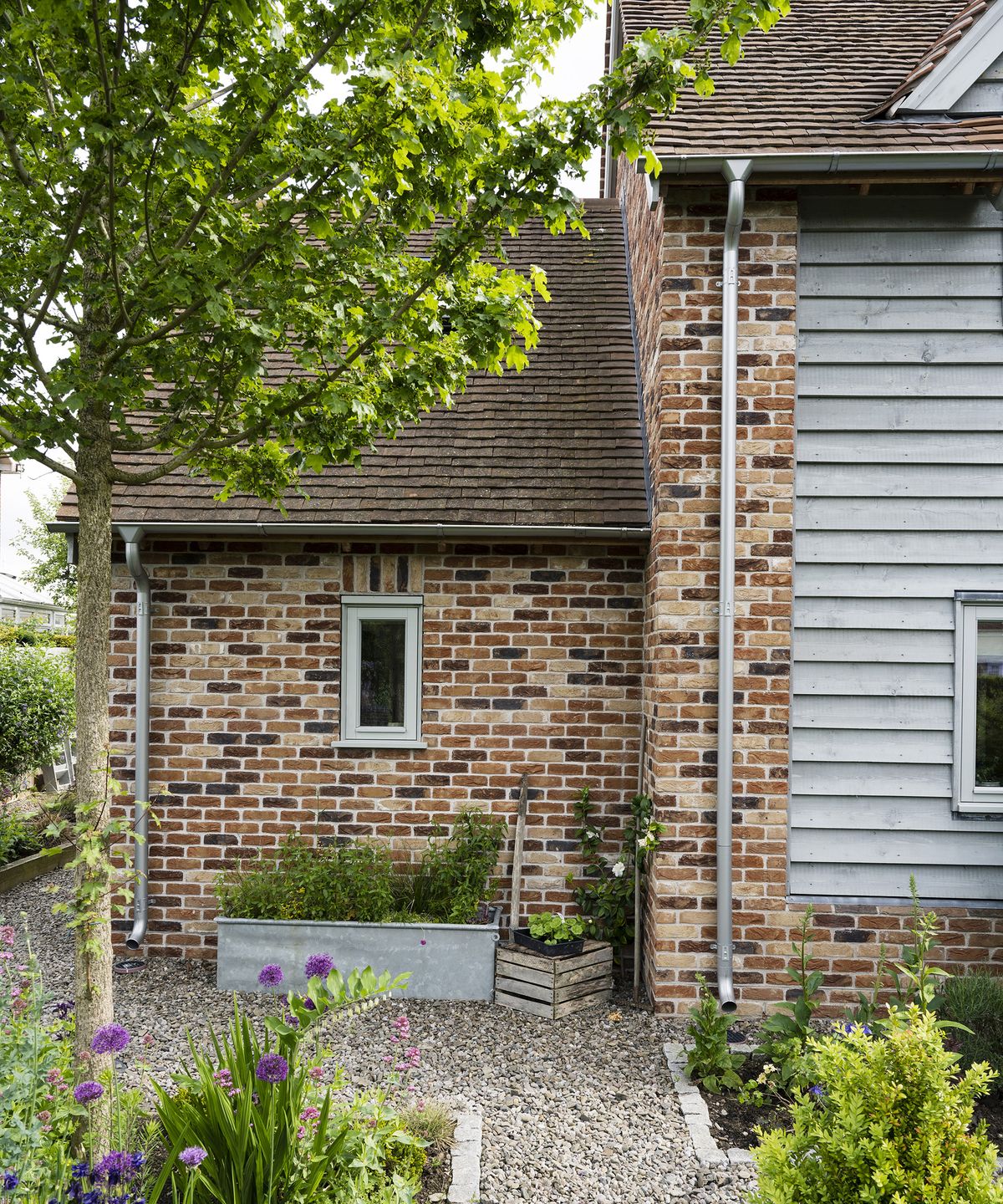 Exterior of a two storey oak frame house with brick and wood cladding with a gravel pathway and spring planting