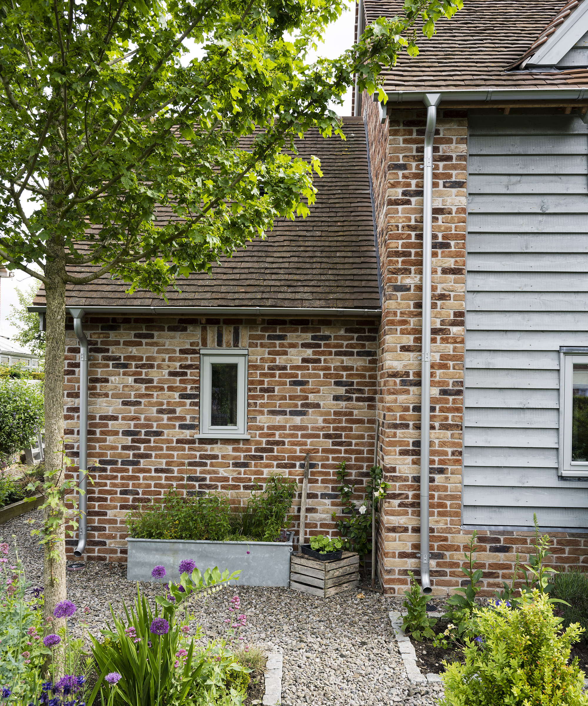 Exterior of a two storey oak frame house with brick and wood cladding with a gravel pathway and spring planting