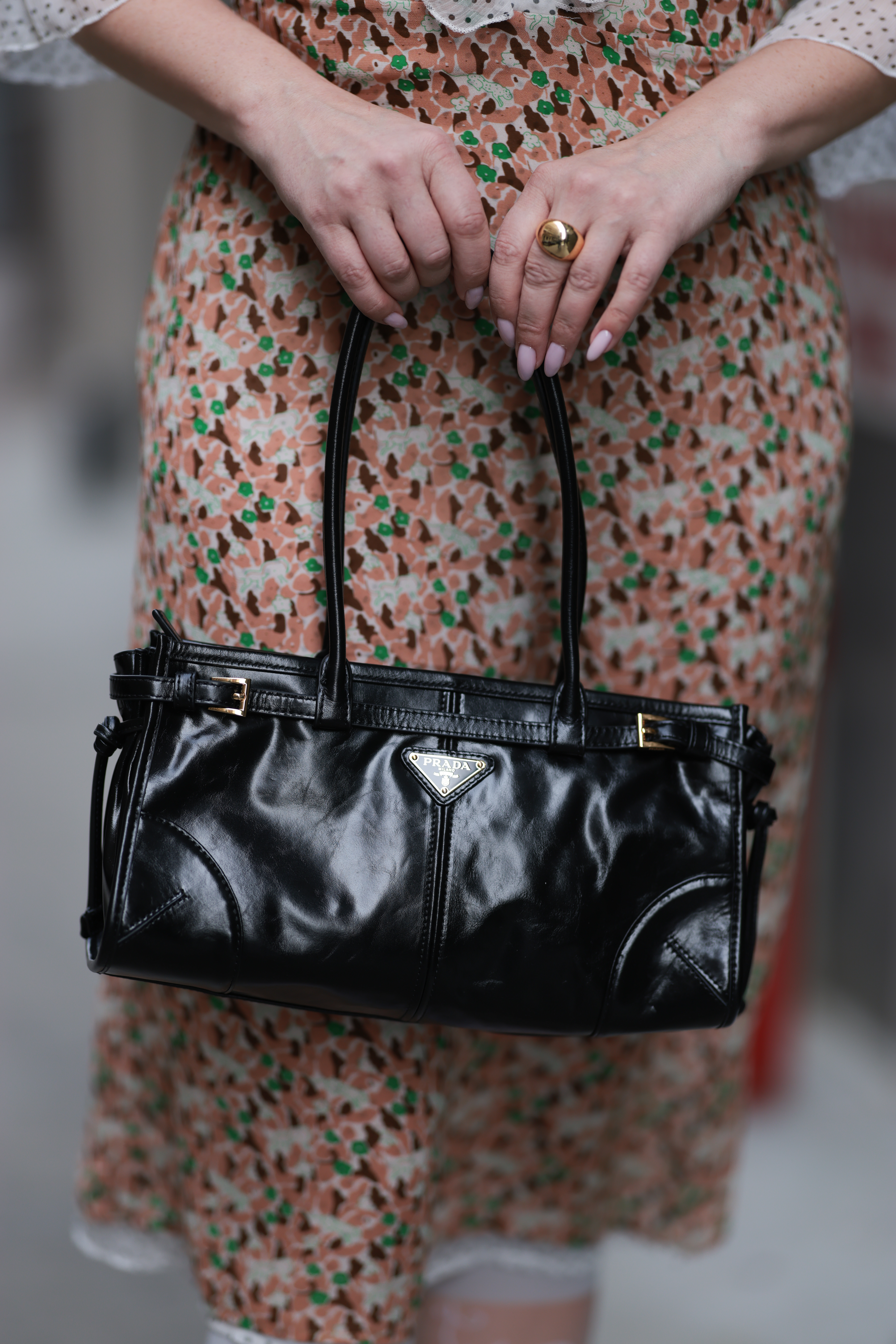 a woman&#039;s hands with a pale pink manicure holding a black leather prada bag over a colorful skirt during new york fashion week