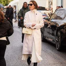 woman wears all white monochromatic outfit with white handbag and black tall boots.