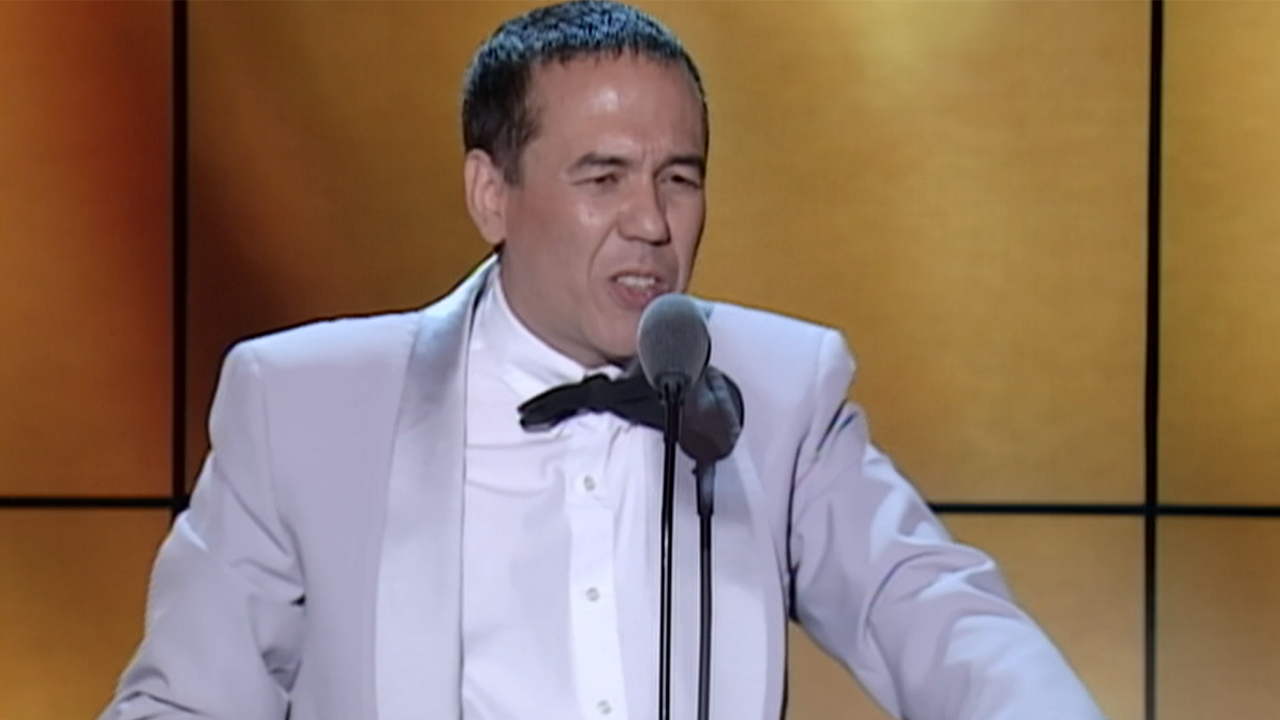 Gilbert Gottfried in a suit, standing in front of a microphone telling a joke in The Aristocrats