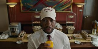 Da 5 Bloods Jonathan Majors holding an orange juice in front of the hotel buffet