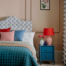 Striped lamp on bobbin bedside table next to bed with matching striped pillows.