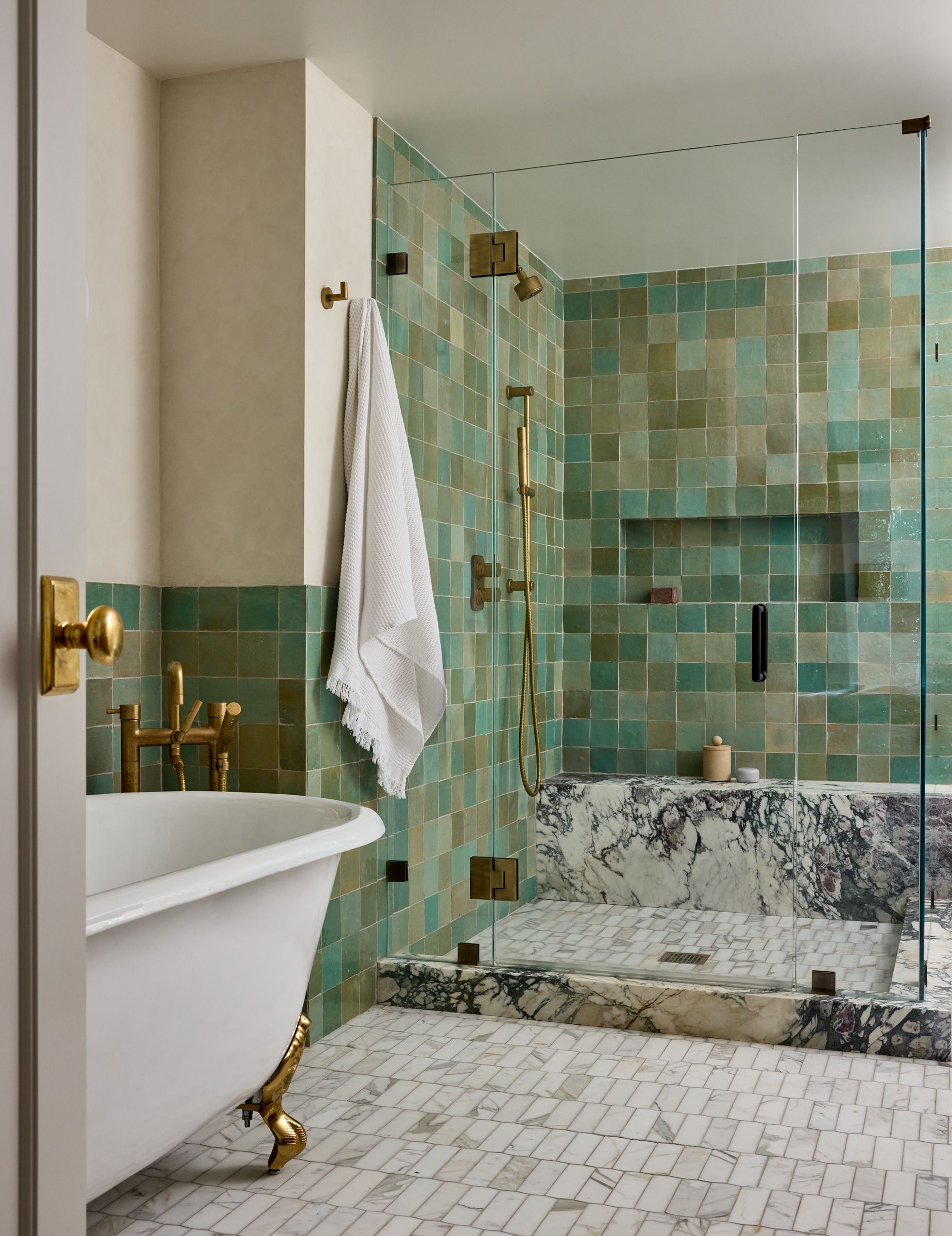 A bathroom with a large shower iwth green square tiles, a marble platform and white and grey floor tiles.