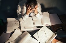 A man holds his head in his hands while looking at some papers.