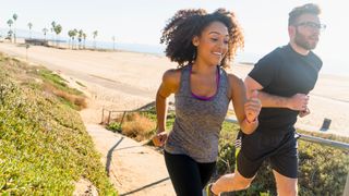 A man and woman smile as they run outdoors by a beach