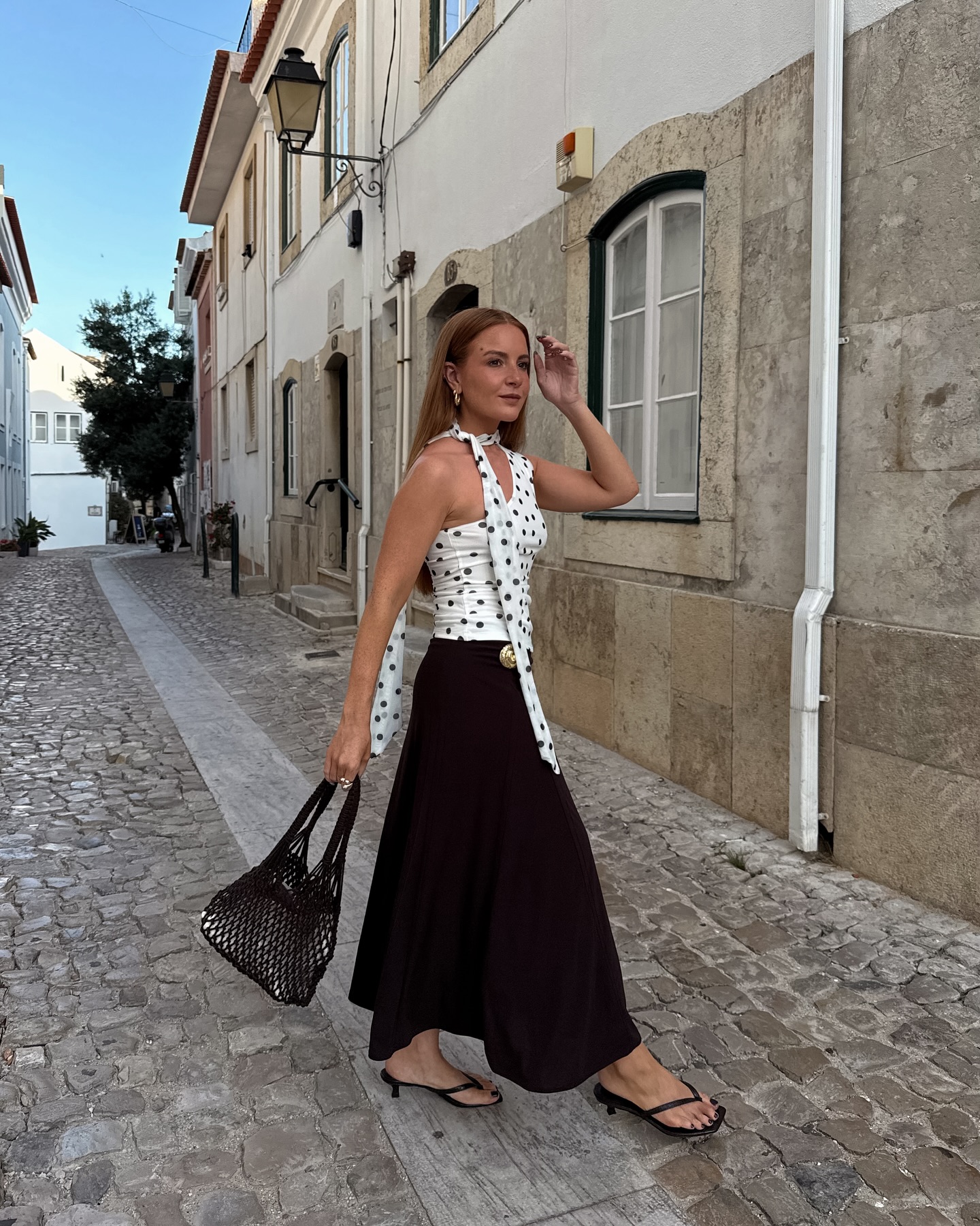 An image of @rebeccaferrazwyatt wearing a polka-dot top with a black maxi skirt while in Portugal.