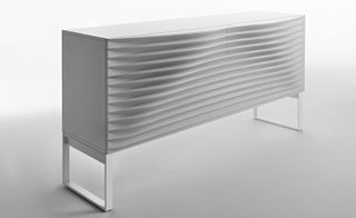 A white horizontal rectangular drawer featuring a ripple effect front and 2 open square legs photographed from the left angle agasint a grey background