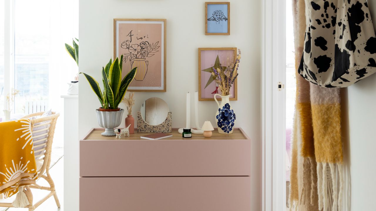 White painted hallway with pink dresser decorated with decorative items and artwork hanging