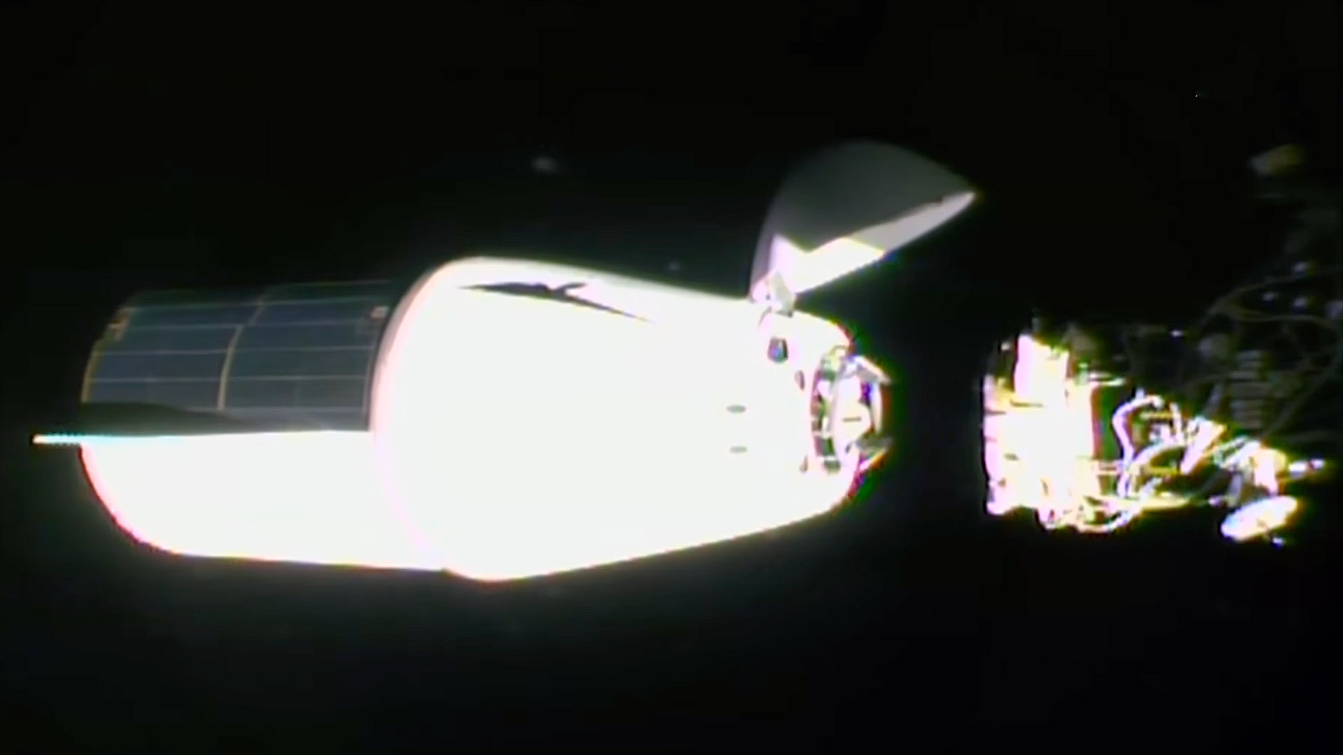 a white spacecraft with a solar array panel covering one half of its trunk approaches docking with a space station