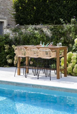 Wicker and black metal bar stools between a swimming pool and a bed of hydrangeas, illustrating outdoor patio furniture ideas.