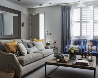 A gray living room with gray sofa, blue drapes and pair of blue armchairs around a wooden coffee table.
