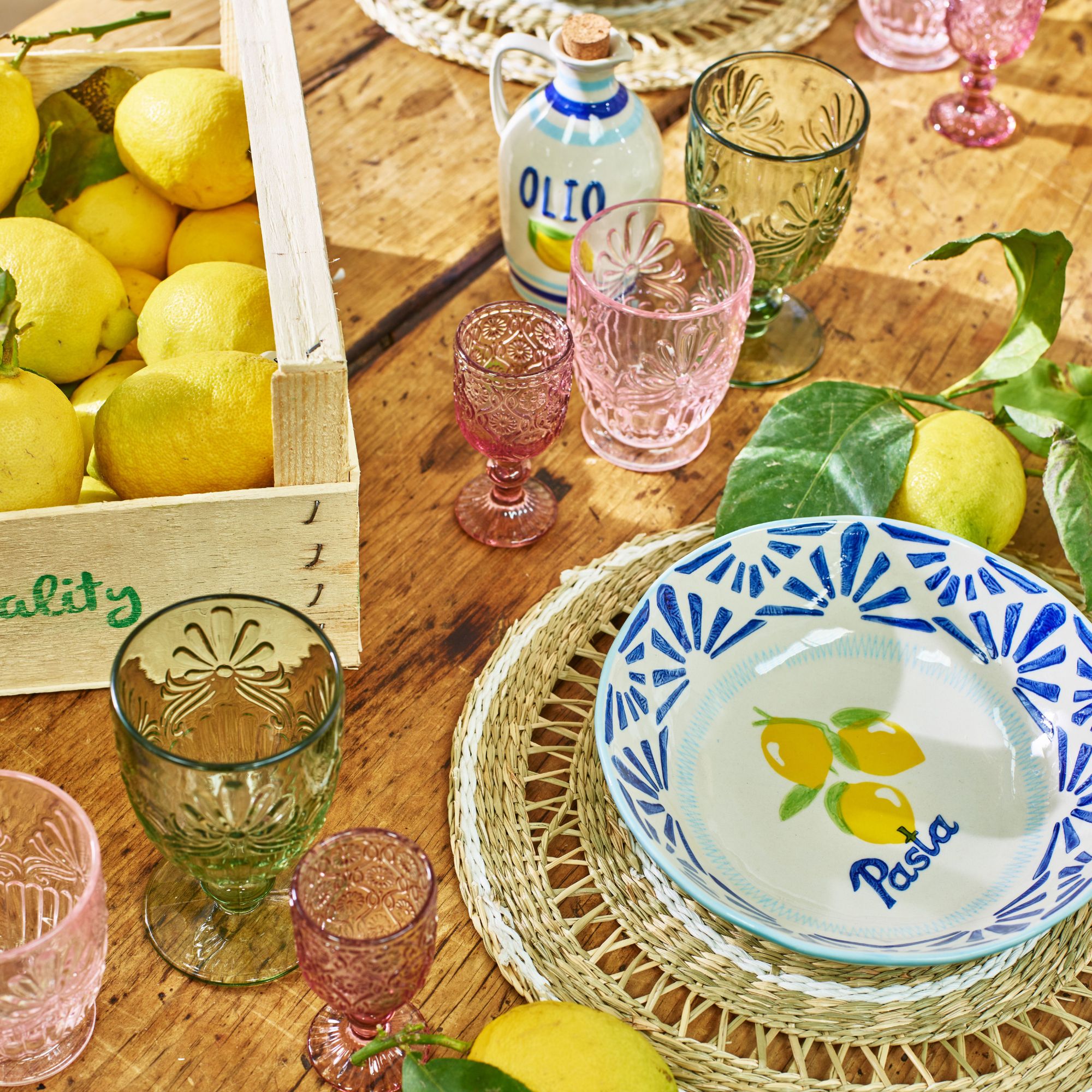 Pink and green glassware on a wooden table with a blue and white bowl and an olive oil jug