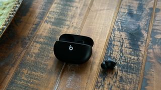 The Beats Studio Buds and their charging case in black on a wooden surface.