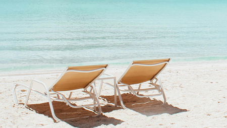 two beach chairs on sand facing the sea