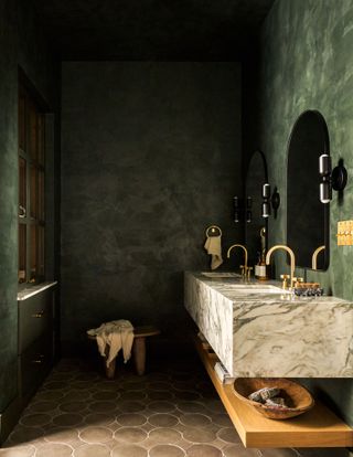 Bathroom with green plaster effect walls, terracotta floor tiles, white marble sink and gold hardware
