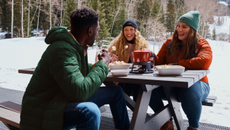 A group of people sitting on a bench wearing a selection of clothing available from Eddie Bauer.