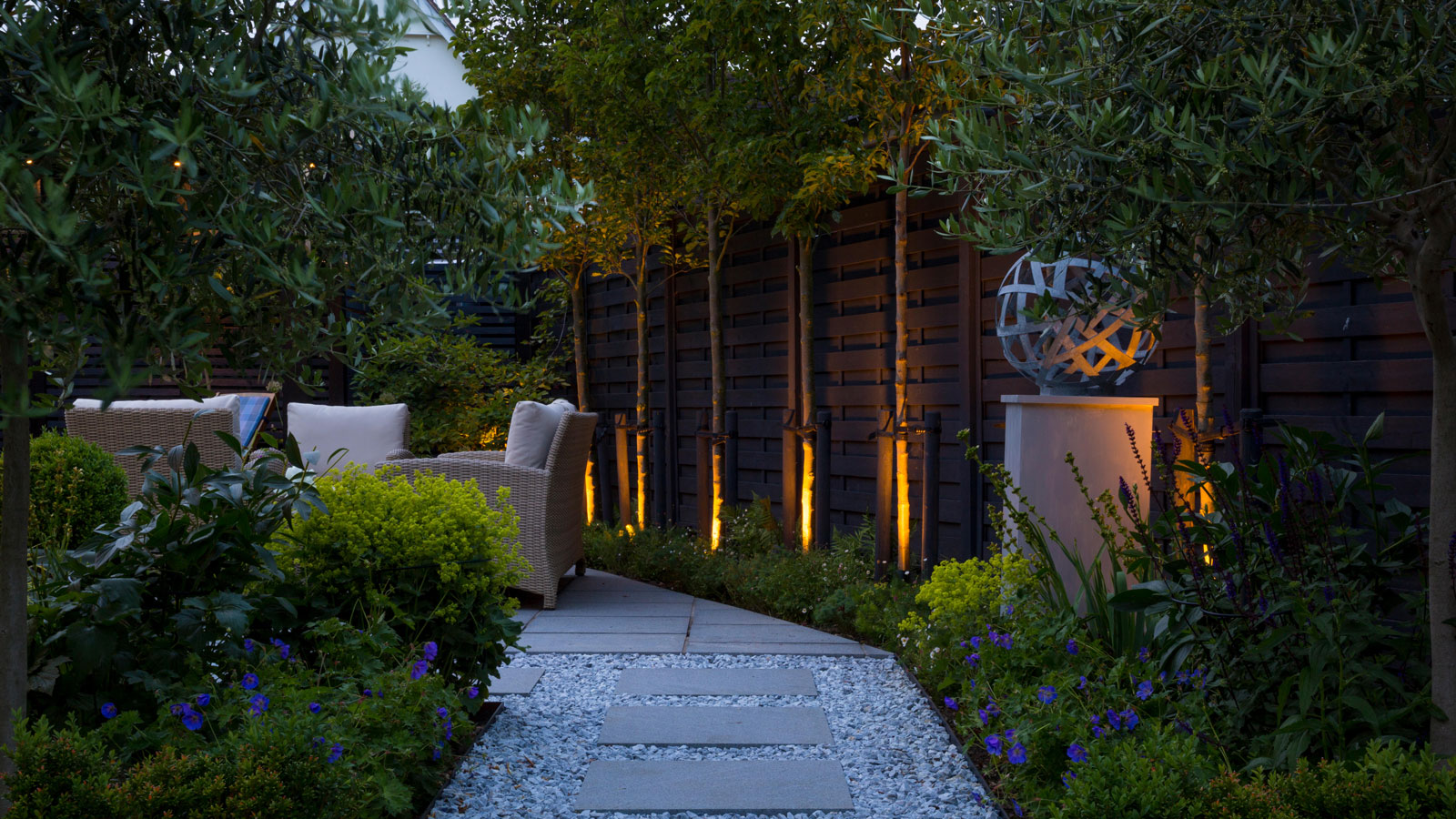 gardening lighting design with pleached trees and sculpture, with garden furniture, gravel pathway and planting beds