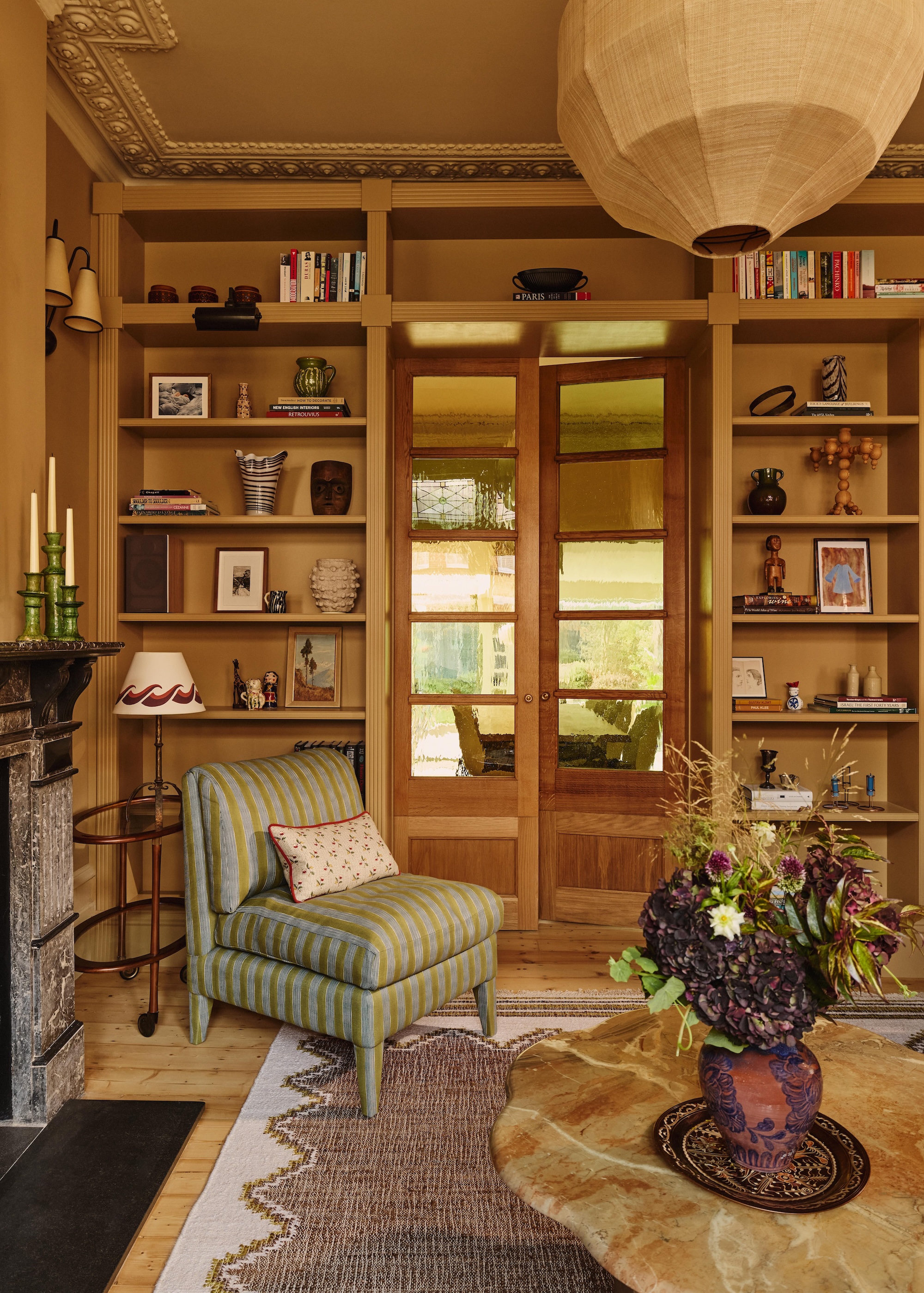 a classic style living room with floor to ceiling shelving around an internal door, a striped accent chair and marble topped coffee table