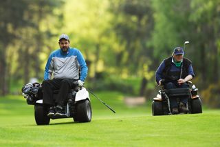 Two golfers in mobility carts drive down the fairway