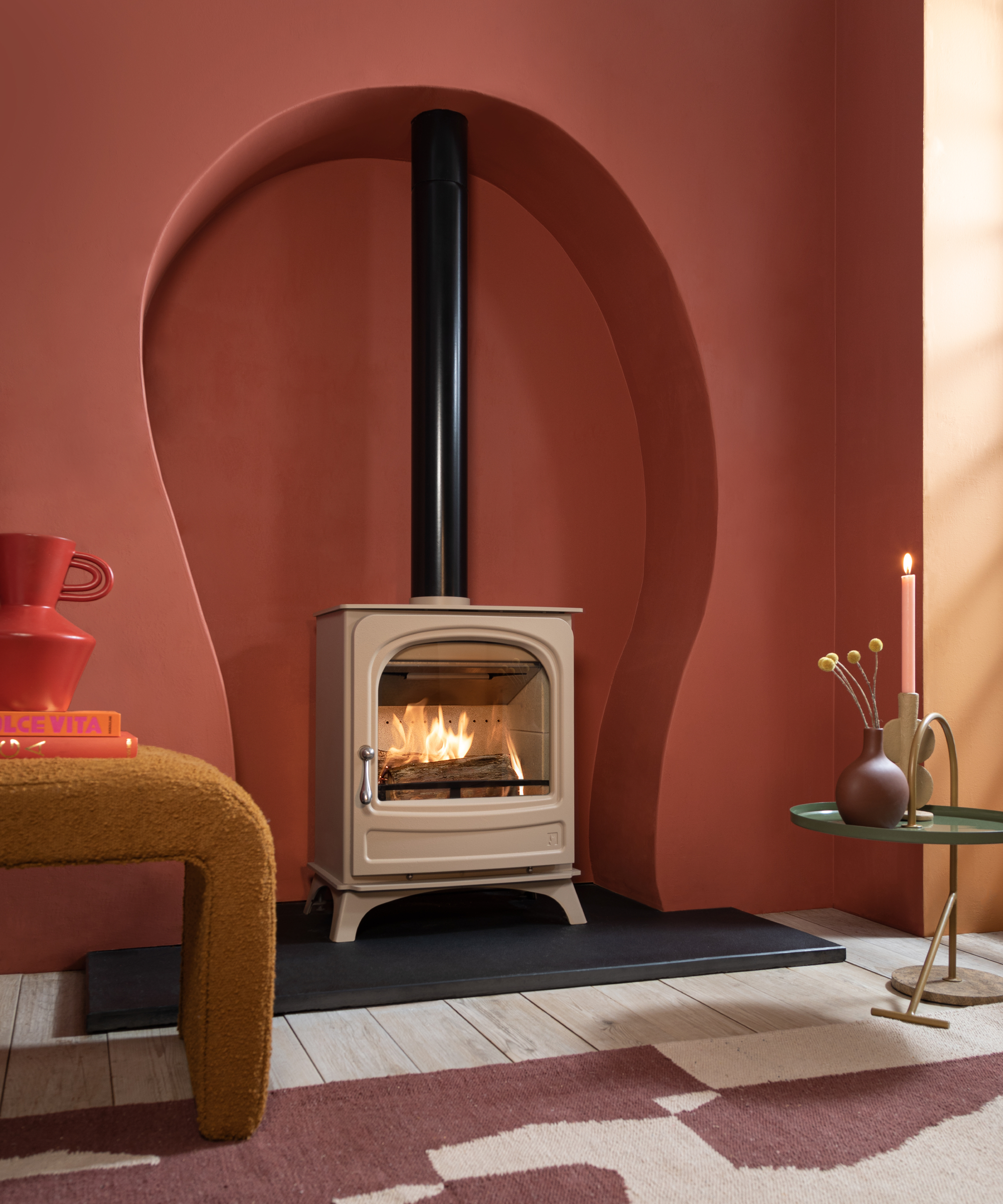 taupe coloured log burner stood on a black hearth located in large curved opening cut into wall painted terracotta