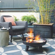 A black and white tiled patio with rattan chair and outdoor fire pit