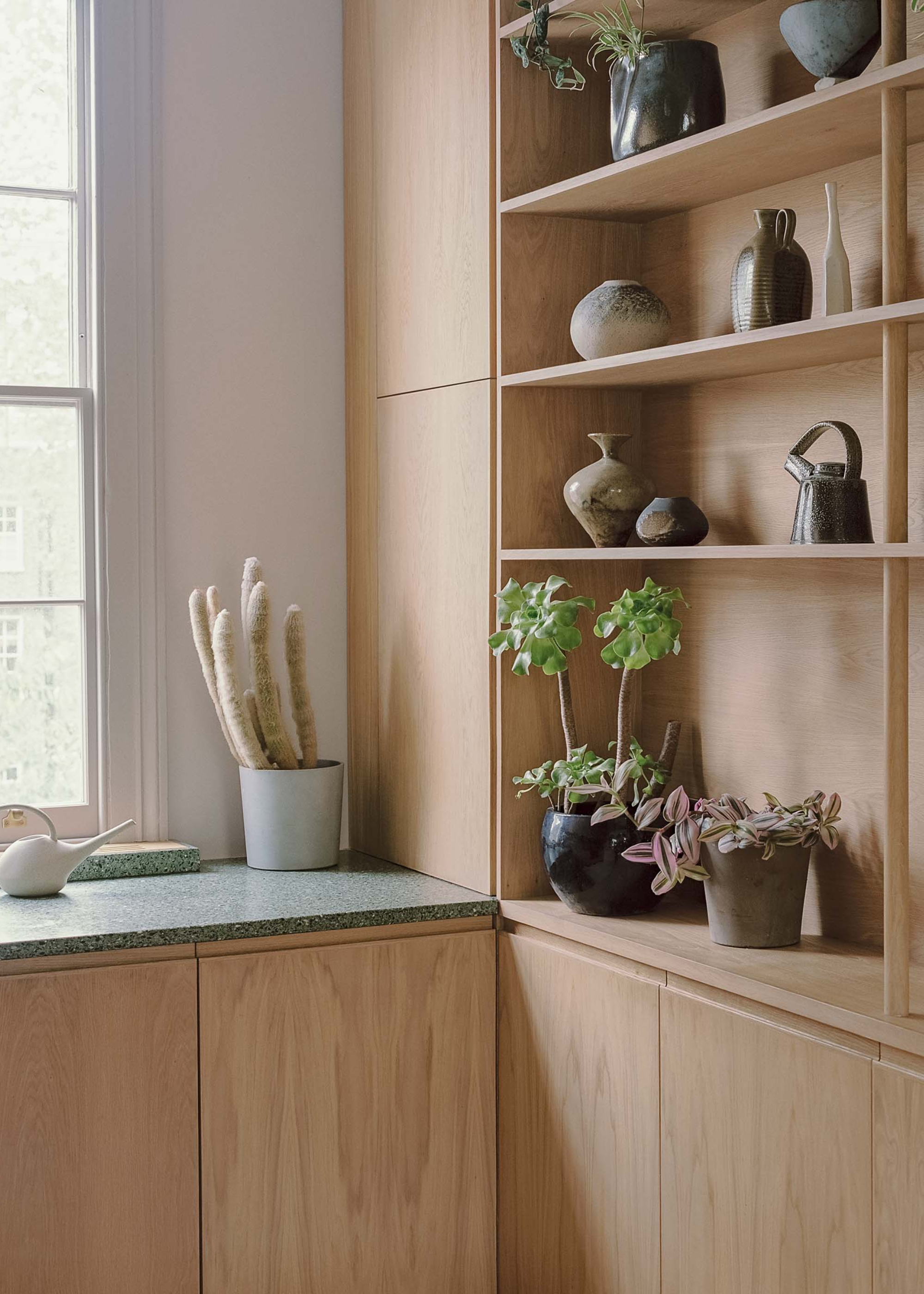 corner of a tiny kitchen with oak cabinetry and open shelving filled with small ceramic objects