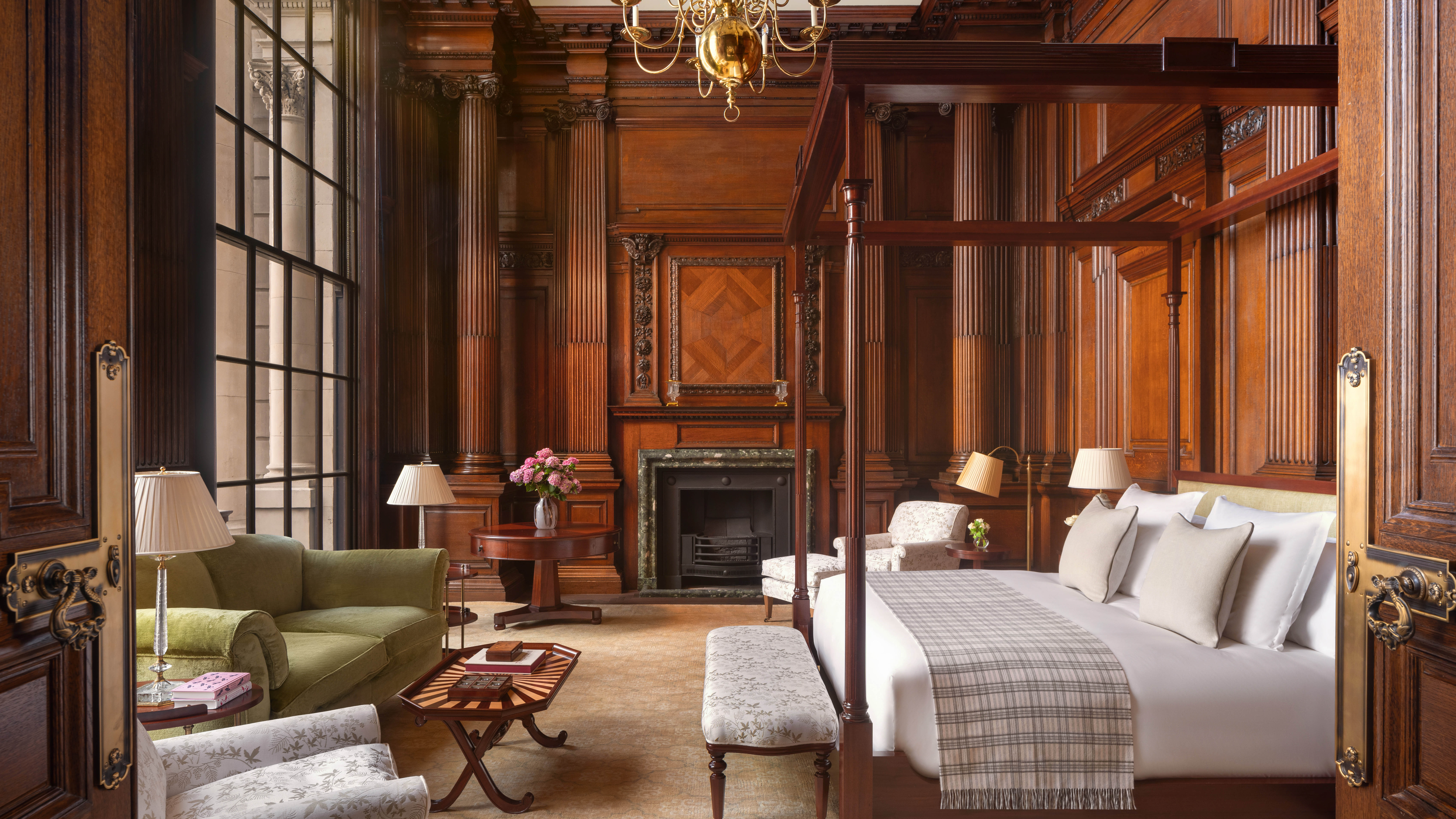 Wood panelled bedroom with a four poster bed, fireplace and green sofa