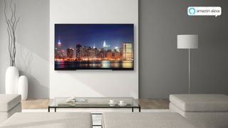 An LCD TV hanging on a wall in a grey living room with a cityscape displayed on the screen.