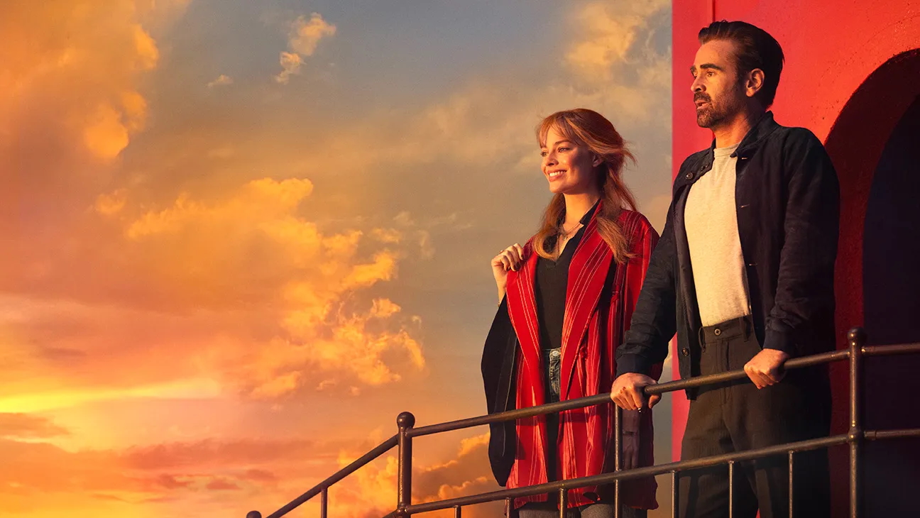 Two people (Margot Robbie and Colin Farrell) look out over the sunset horizon as they stand at the top of a lighthouse, in the romance movie 'A Big Bold Beautiful Journey.'
