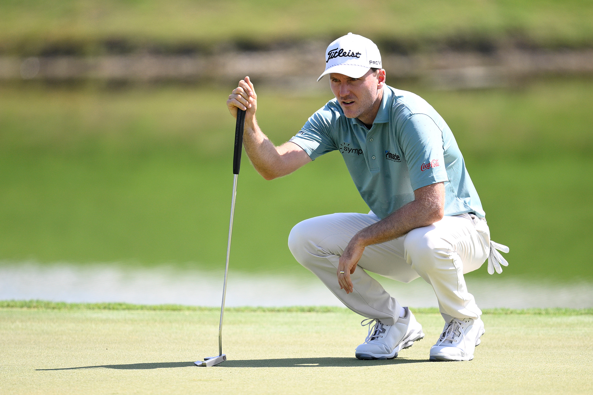 Russell Henley reading a putt while crouching down on the green and leaning on his putter