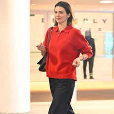 Kendall Jenner wears a red sweater, black shoulder bag, black jeans, white socks, and black The Row loafers.