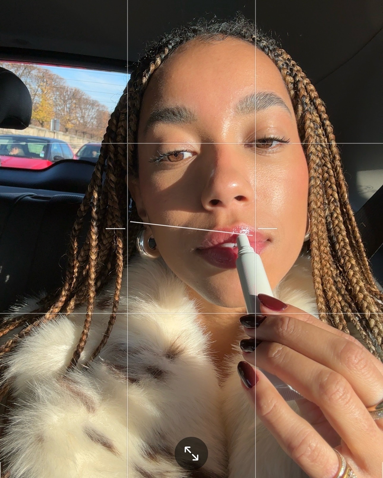 A woman applying a glossy lip product in the back of a car