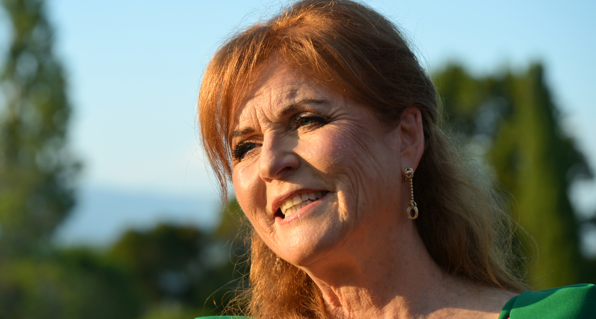 Sarah Ferguson smiling outside in a green and pink dress