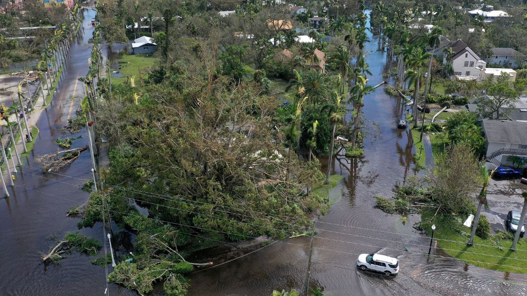 aerial shot of a flooded neighborhood and a car driving through the wreckage in Fort Myers, Florida after a hurricane hit