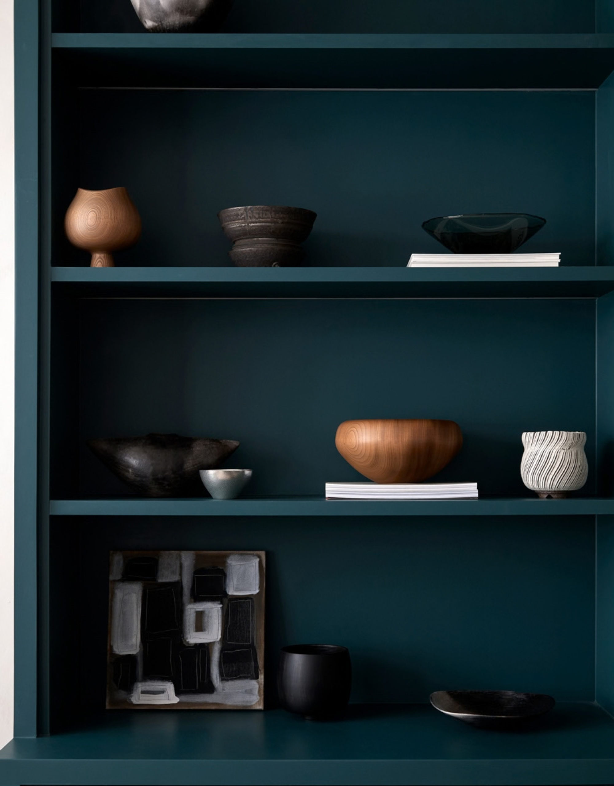 An open display of dark green shelves with ceramics and crafts on display