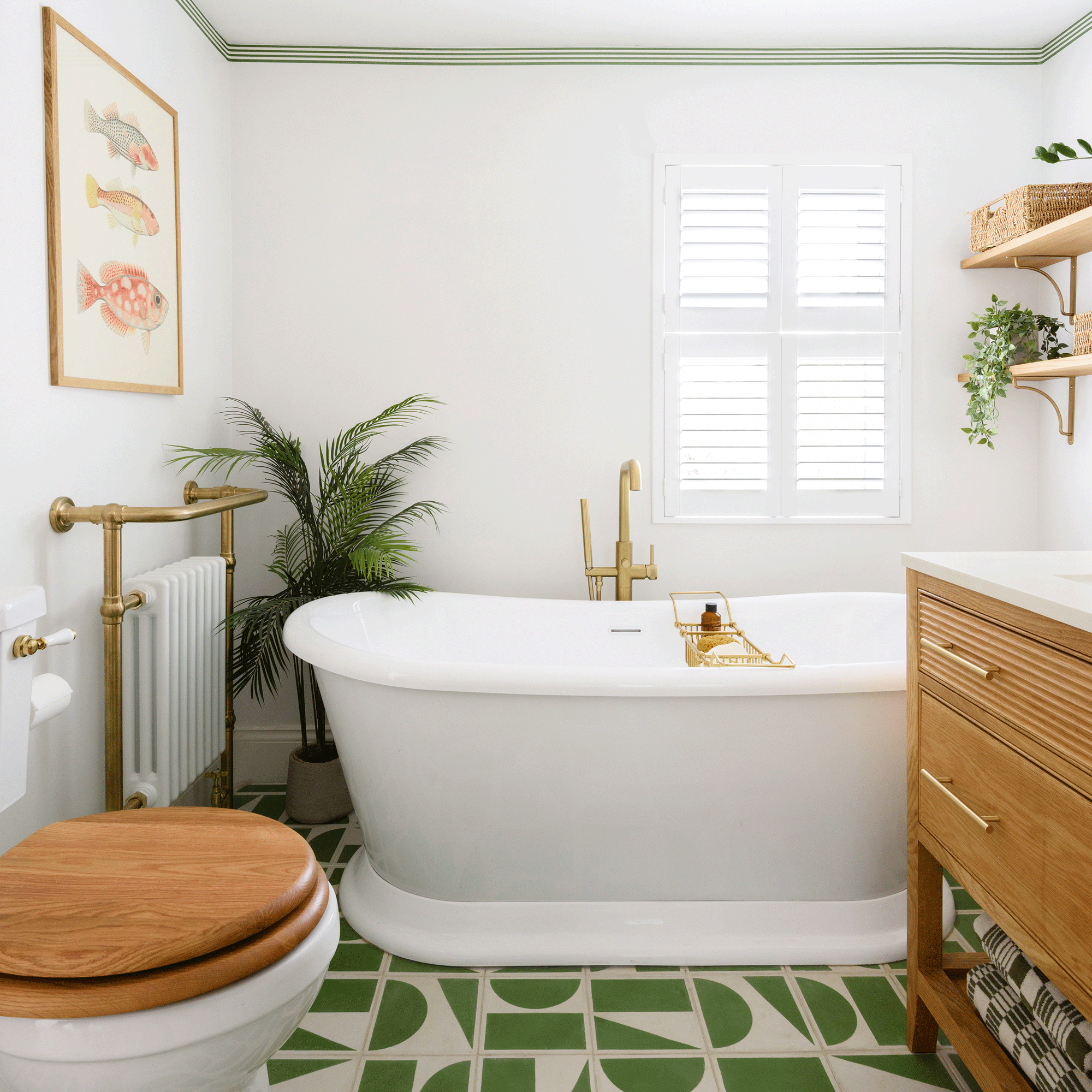 a small white bathroom with green and cream tiled patterned flooring, with a loo, freestanding bath and radiator with towel rail