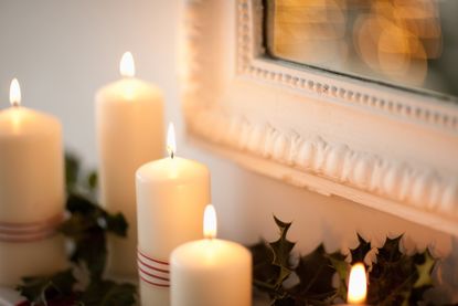 Candles lit on mantlepiece next to a mirror with holly in the background